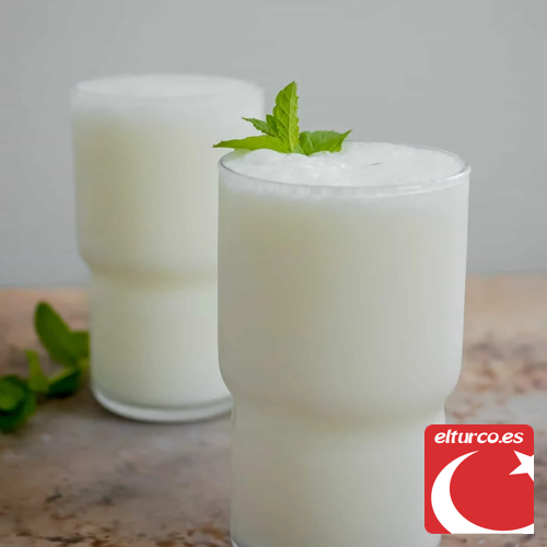 Vaso y jarra de vidrio con una bebida blanca y espumosa similar al ayran