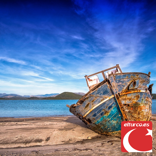 Casco de madera de un viejo barco naufragado sobre una playa de arena, con el mar y las montañas al fondo