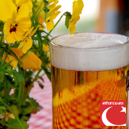 Jarra de cerveza rubia con espuma junto a unas flores amarillas en una mesa de terraza
