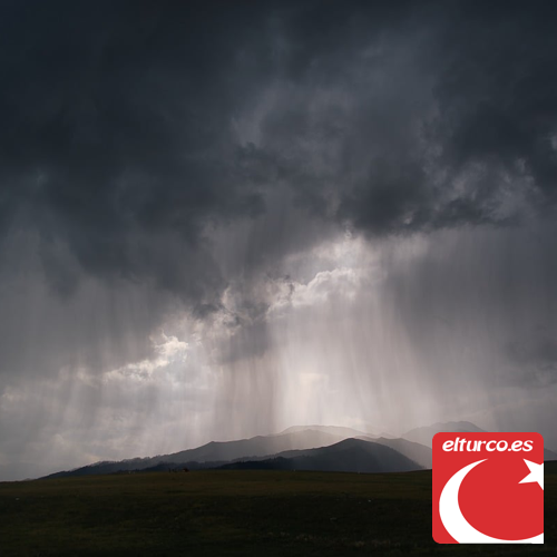 Tormenta con lluvia torrencial cayendo desde nubes oscuras sobre unas montañas, con un rayo de luz entre las nubes
