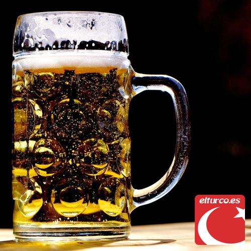 Jarra de cerveza dorada con espuma sobre una mesa, a contraluz y con fondo oscuro