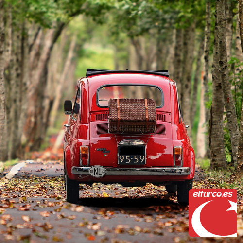 Fiat 500 rojo clásico visto de espaldas en una carretera de árboles con hojas otoñales