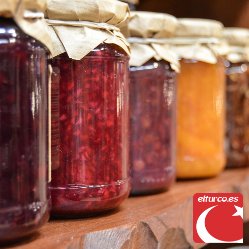 Hilera de tarros de mermelada artesanal de frutas rojas y naranjas sobre una balda de madera